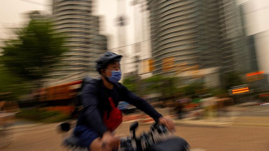Seseorang mengenakan masker saat bersepeda, sementara asap kebakaran hutan dari Ontario barat laut memenuhi langit, ditambah dengan gelombang panas yang hebat, memicu peringatan kesehatan dan seruan kepada warga untuk membatasi aktivitas di luar ruangan di Toronto, Ontario, Kanada, 15 Juli 2026.