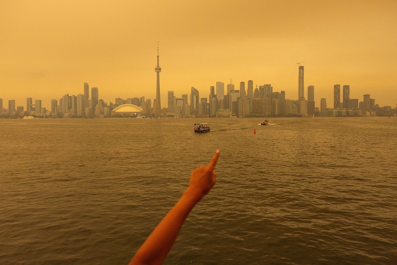 Seseorang menunjuk ke cakrawala saat menaiki feri dari Pulau Toronto, sementara asap kebakaran hutan dari Ontario barat laut memenuhi langit, ditambah dengan gelombang panas yang hebat, memicu peringatan kesehatan dan seruan kepada warga untuk membatasi aktivitas di luar ruangan di Toronto, Ontario, Kanada, 15 Juli 2026. (REUTERS/Carlos Osorio)
