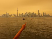 Seseorang menunjuk ke cakrawala saat menaiki feri dari Pulau Toronto, sementara asap kebakaran hutan dari Ontario barat laut memenuhi langit, ditambah dengan gelombang panas yang hebat, memicu peringatan kesehatan dan seruan kepada warga untuk membat