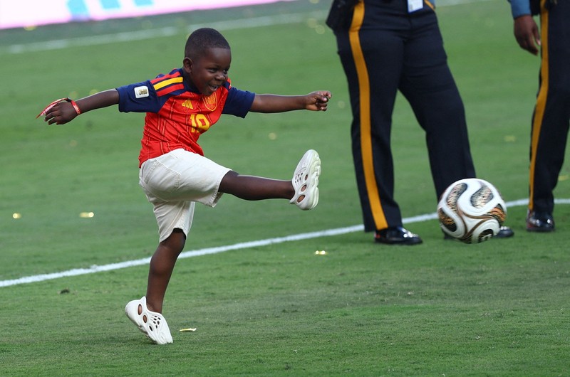 Lamine Yamal merayakan keberhasilan Spanyol menjuarai Piala Dunia FIFA 2026, sementara adiknya, Keyne Yamal, bermain sepak bola di lapangan usai seremoni penyerahan trofi di New York/New Jersey Stadium, East Rutherford, New Jersey, Amerika Serikat, Minggu (19/7/2026). (REUTERS/Agustin Marcarian)