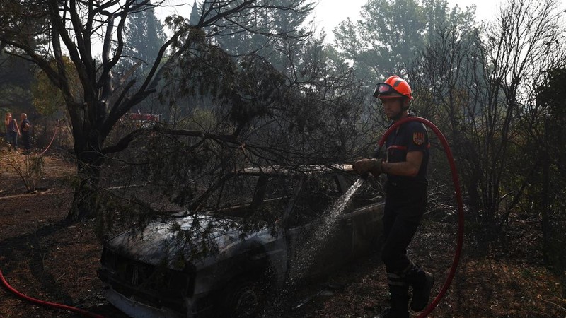 Petugas pemadam kebakaran Prancis menyemprotkan air di dekat mobil yang terbakar selama operasi pembersihan di dekat sebuah rumah yang terbakar di daerah yang terkena dampak kebakaran hutan di Cotignac, di departemen Var, saat kondisi kekeringan memburuk setelah gelombang panas dan kekurangan air di sebagian besar Prancis, 22 Juli 2026.