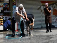 Seorang pekerja toko makanan cepat saji tradisional mencoba mendinginkan seseorang dengan menuangkan air ke kepalanya, di sepanjang Jalan Nakamise di distrik Asakusa, tempat wisata populer, saat pemerintah Jepang mengeluarkan peringatan serangan pana