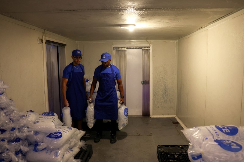 Karyawan Blue Ice, Evans Osagie, memasukkan es batu ke dalam kantong saat gelombang panas di Athena, Yunani, 22 Juli 2026. (REUTERS/Louiza Vradi)