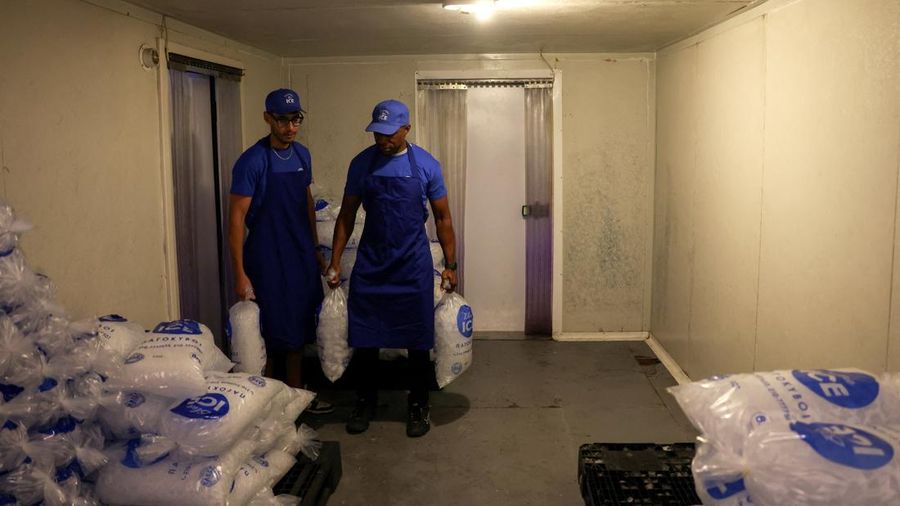 Karyawan Blue Ice, Aziz Lasnami dan Evans Osagie, membawa kantong-kantong es batu di fasilitas perusahaan selama gelombang panas di Athena, Yunani, 22 Juli 2026.