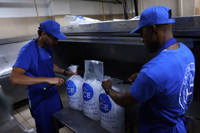 Karyawan Blue Ice, Evans Osagie, memasukkan es batu ke dalam kantong saat gelombang panas di Athena, Yunani, 22 Juli 2026. (REUTERS/Louiza Vradi)