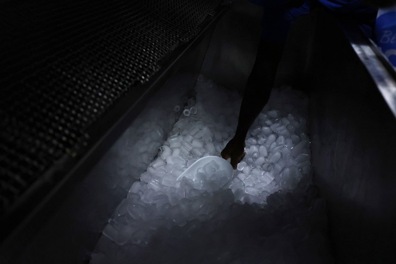 Karyawan Blue Ice, Evans Osagie, memasukkan es batu ke dalam kantong saat gelombang panas di Athena, Yunani, 22 Juli 2026. (REUTERS/Louiza Vradi)