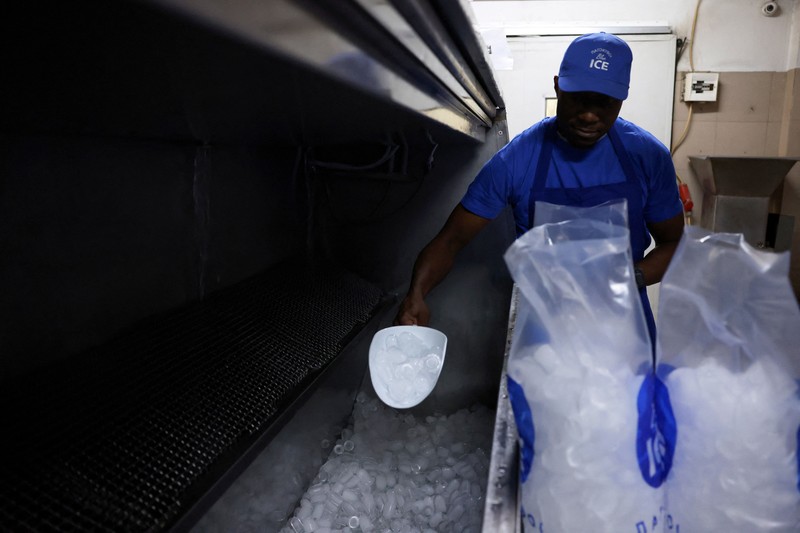 Karyawan Blue Ice, Evans Osagie, memasukkan es batu ke dalam kantong saat gelombang panas di Athena, Yunani, 22 Juli 2026. (REUTERS/Louiza Vradi)