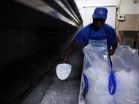 Karyawan Blue Ice, Evans Osagie, memasukkan es batu ke dalam kantong saat gelombang panas di Athena, Yunani, 22 Juli 2026. (REUTERS/Louiza Vradi)