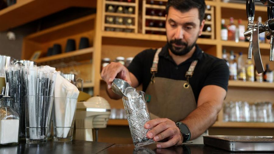 Seorang bartender menambahkan es batu dari perusahaan lokal Blue Ice ke dalam minuman di sebuah kafe selama gelombang panas di Athena, Yunani, 22 Juli 2026.