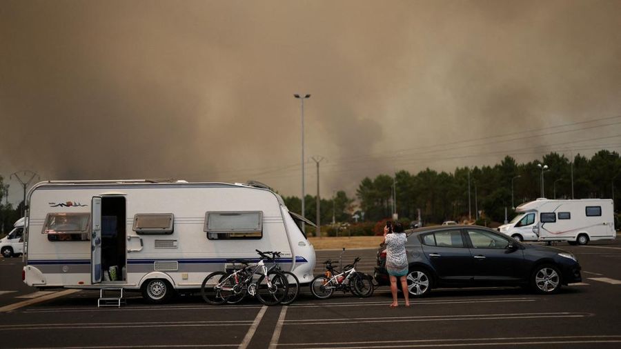 Seorang turis yang dievakuasi dari perkemahan mengambil foto kebakaran hutan sambil berdiri di samping mobil dan karavannya yang diparkir di tempat parkir supermarket di Ares, saat kebakaran hutan terus melanda area hutan dekat Bassin d'Arcachon di departemen Gironde di tengah memburuknya kondisi kekeringan setelah gelombang panas dan kekurangan air di sebagian besar Prancis, 23 Juli 2026.