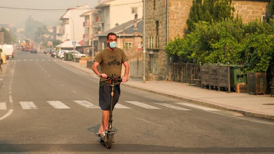 Seseorang yang mengenakan masker mengendarai skuter listrik menembus asap akibat kebakaran hutan di Navaluenga, Avila, Spanyol, 23 Juli 2026.