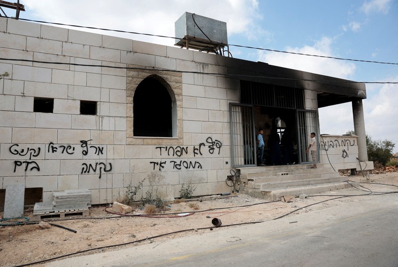 Anak-anak muda Palestina berdiri di depan sebuah masjid yang rusak, yang menurut warga Palestina dirusak oleh pemukim Israel, di Qusra dekat Nablus, di Tepi Barat yang diduduki Israel, 26 Juli 2026. Grafiti di dinding termasuk