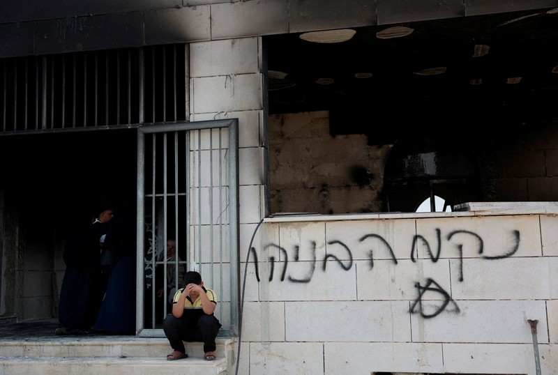 Anak-anak muda Palestina berdiri di depan sebuah masjid yang rusak, yang menurut warga Palestina dirusak oleh pemukim Israel, di Qusra dekat Nablus, di Tepi Barat yang diduduki Israel, 26 Juli 2026. Grafiti di dinding termasuk
