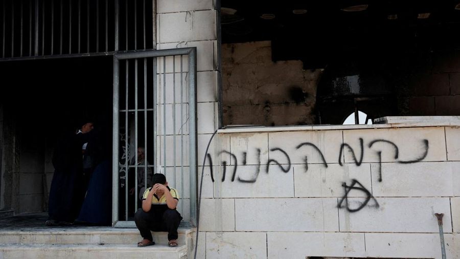 Seorang anak laki-laki Palestina duduk di dekat masjid yang rusak, yang menurut warga Palestina dirusak oleh pemukim Israel, di Qusra dekat Nablus, di Tepi Barat yang diduduki Israel, 26 Juli 2026. Grafiti di dinding bertuliskan