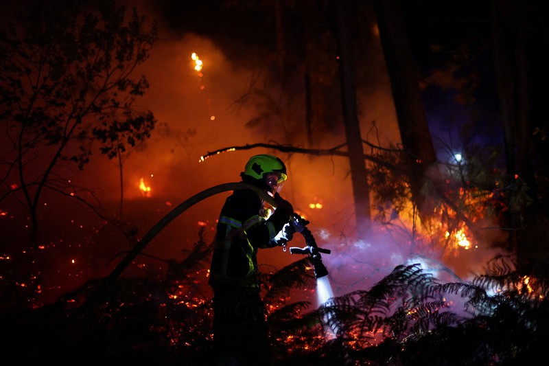 Seorang pria dan anjingnya melihat kebakaran hutan di pegunungan di Onda, Spanyol, 27 Juli 2026. (REUTERS/Pedro Nunes)