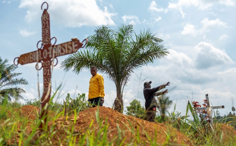 Charles Mambo, the supervisor at the Ceca-20 cemetery, flanked by Moise Mund'wa, the assistant warden of the cemetery, talks near graves during an interview with Reuters, as aid agencies intensify efforts to contain an Ebola outbreak caused by the Bundibugyo virus, in the Ebola hit Mungwalu, Djugu Territory of Ituri province, Democratic Republic of Congo, July 14, 2026. REUTERS/Gradel Muyisa Mumbere     TPX IMAGES OF THE DAY