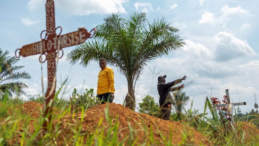 Charles Mambo, the supervisor at the Ceca-20 cemetery, flanked by Moise Mund'wa, the assistant warden of the cemetery, talks near graves during an interview with Reuters, as aid agencies intensify efforts to contain an Ebola outbreak caused by the Bu