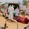 Members of the Civil Protection, a local community-based team that works to help mitigate the spread of the Ebola virus and ensure burials happen safely and quickly, wearing personal protective equipment (PPE), handle a wooden coffin before loading t