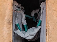 Members of the Civil Protection, a local, community-based team that helps lower resistance and ensures burials happen safely and quickly, while wearing personal protective equipment (PPE), carry a body bag with the remains of an unidentified man who,