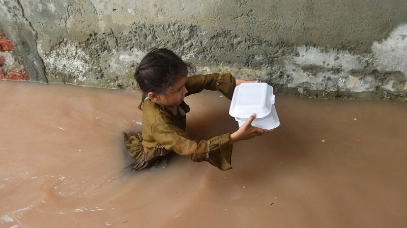 Seorang gadis membawa bungkusan makanan sambil menerobos genangan air banjir setelah hujan monsun di Ferozwala, Pakistan, 28 Juli 2026.