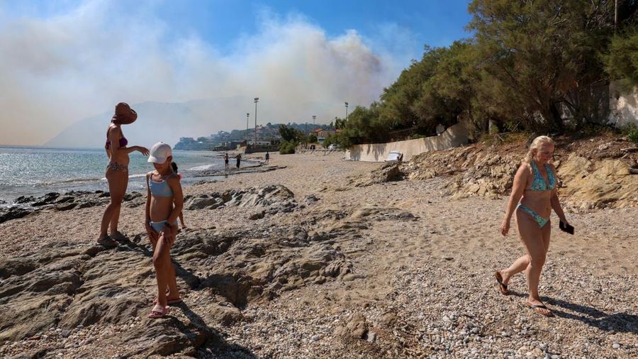 Orang-orang berjalan di pantai sementara asap mengepul dari kebakaran hutan yang terjadi di dekat desa Plomari di pulau Lesbos, Yunani, 29 Juli 2026.