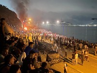 Migrants gather around a torched vehicle while waiting for a chance to cross to the Spanish enclave of Ceuta, on the Moroccan side of the border in Fnideq, Morocco, July 31, 2026. Picture taken with a mobile phone.   REUTERS/Ahmed El Jechtimi     TPX