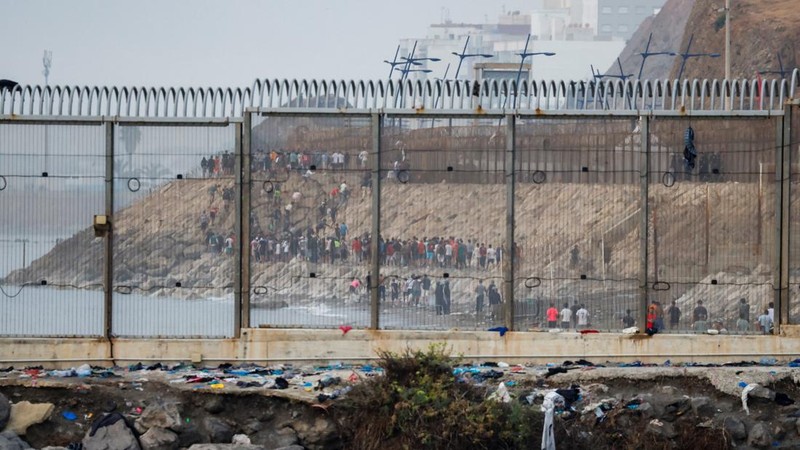 Migrants walk on the Moroccan side of the border, after mass crossings of migrants on foot and by sea from Morocco into Spanish territory, as seen from Cueta, Spain, August 1, 2026. REUTERS/Jon Nazca