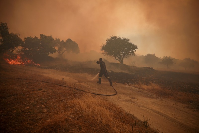 Seorang warga menyaksikan sebuah helikopter menjatuhkan air saat kebakaran hutan melanda lembah Megara, Yunani, 2 Agustus 2026. (REUTERS/Louisa Gouliamaki)