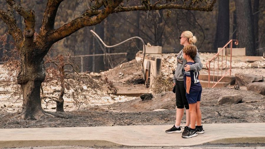 Jana Jensen mengamati lingkungan tempat rumah masa kecilnya, yang dimiliki oleh orang tuanya, hangus terbakar akibat kebakaran hutan, sambil memeluk putranya, Aaren, 8 tahun, di Spokane, Washington, AS, 2 Agustus 2026.