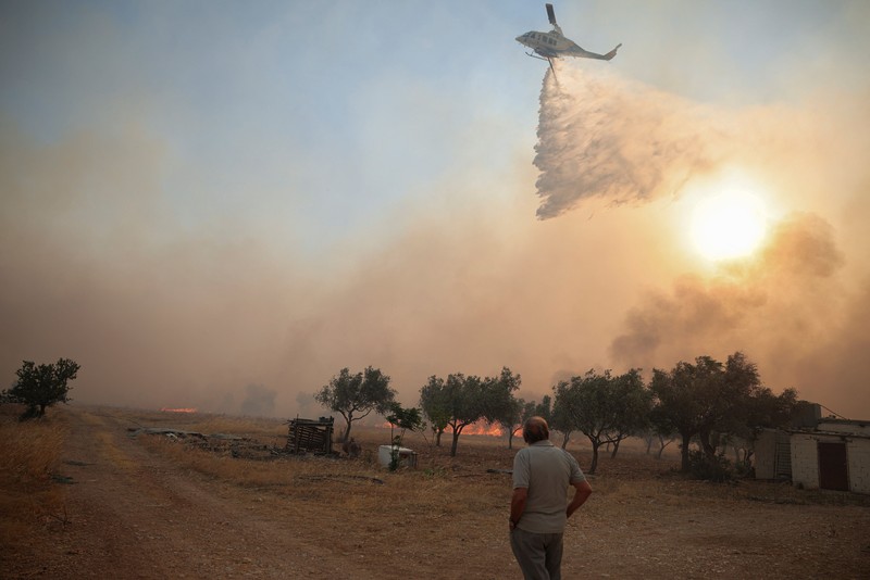 Seorang warga menyaksikan sebuah helikopter menjatuhkan air saat kebakaran hutan melanda lembah Megara, Yunani, 2 Agustus 2026. (REUTERS/Louisa Gouliamaki)