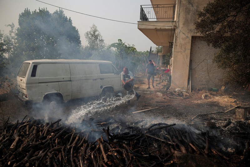 Seorang warga menyaksikan sebuah helikopter menjatuhkan air saat kebakaran hutan melanda lembah Megara, Yunani, 2 Agustus 2026. (REUTERS/Louisa Gouliamaki)