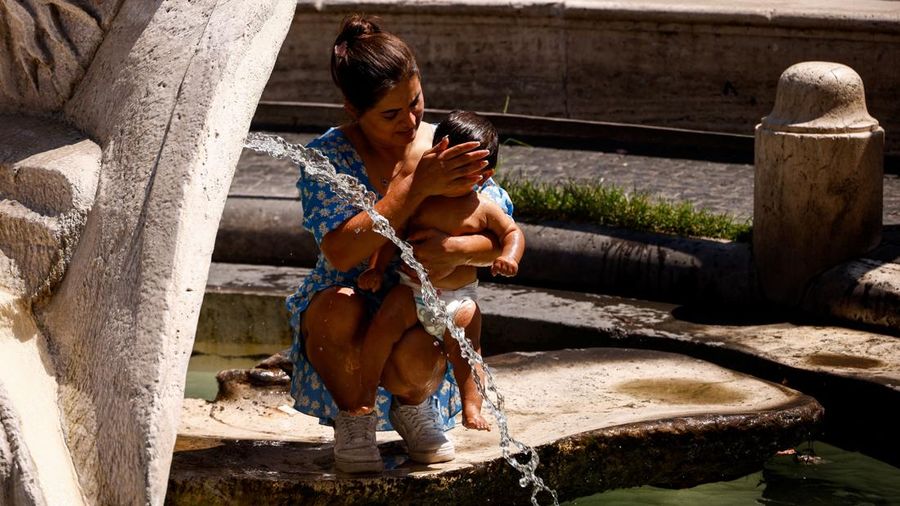 Seorang wanita menggendong bayi di dekat aliran air di Fontana della Barcaccia saat gelombang panas melanda Roma, Italia, pada 6 Agustus 2026.