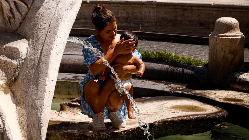 Seorang wanita menggendong bayi di dekat aliran air di Fontana della Barcaccia saat gelombang panas melanda Roma, Italia, pada 6 Agustus 2026.