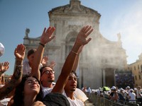 Warga mengangkat tangan sembari menyejukkan diri di tengah semburan kabut air di luar Basilika Santa Maria degli Angeli saat berkumpul untuk menyambut kunjungan Paus Leo dalam rangka peringatan 800 tahun wafatnya Santo Fransiskus, di tengah gelombang