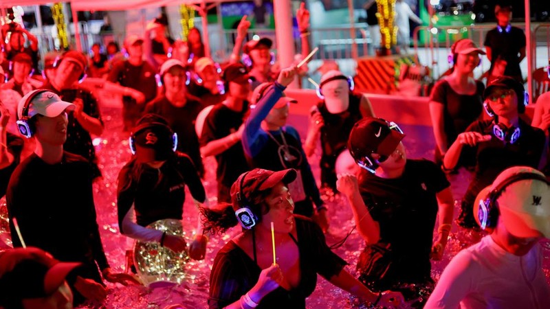 Orang-orang yang mengenakan headphone nirkabel menari di dalam kolam untuk menyejukkan diri saat acara