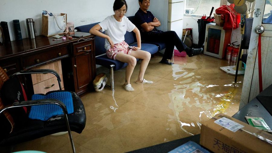 Orang-orang duduk di sofa di dalam ruangan yang terendam banjir setelah Topan Dolphin membawa hujan lebat ke Shanghai, Tiongkok, pada 10 Agustus 2026.