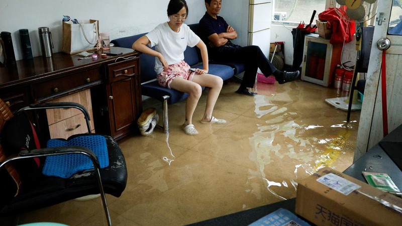 Orang-orang duduk di sofa di dalam ruangan yang terendam banjir setelah Topan Dolphin membawa hujan lebat ke Shanghai, Tiongkok, pada 10 Agustus 2026.