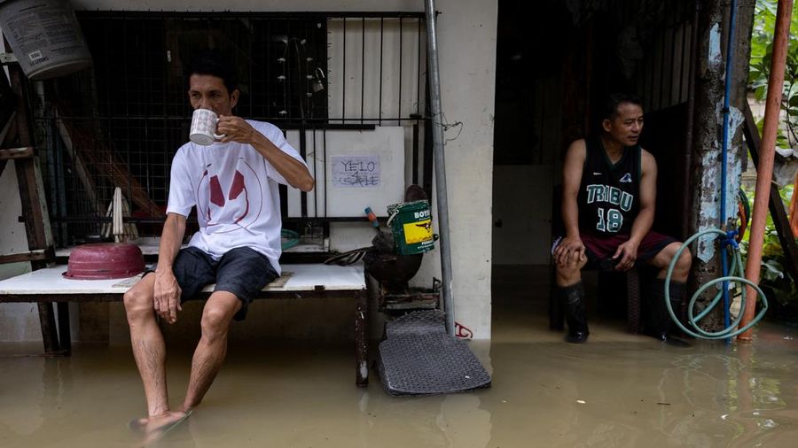 Rolly Gatan minum kopi bersama tetangganya, Jair Paredes, sembari duduk di rumah Paredes yang terendam banjir akibat hujan monsun barat daya di Bagong Silangan, Quezon City, Filipina, pada 10 Agustus 2026.