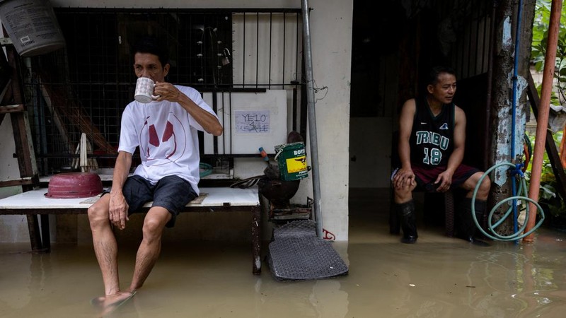 Rolly Gatan minum kopi bersama tetangganya, Jair Paredes, sembari duduk di rumah Paredes yang terendam banjir akibat hujan monsun barat daya di Bagong Silangan, Quezon City, Filipina, pada 10 Agustus 2026.