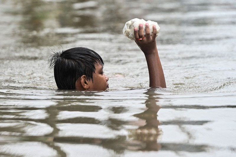 Warga yang membawa barang-barang mereka berjalan menerjang banjir di sebuah desa di tengah hujan monsun barat daya di Bagong Silangan, Quezon City, Filipina, pada 10 Agustus 2026. (REUTERS/Eloisa Lopez)