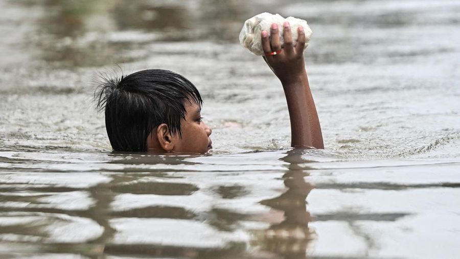 Seorang anak laki-laki memegang lumpia mentah saat berjalan menerjang banjir setelah hujan deras semalam di Barangay Marulas, Kawit, Cavite, Filipina, pada 9 Agustus 2026.