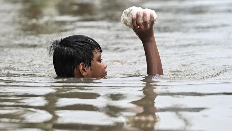 Seorang anak laki-laki memegang lumpia mentah saat berjalan menerjang banjir setelah hujan deras semalam di Barangay Marulas, Kawit, Cavite, Filipina, pada 9 Agustus 2026.