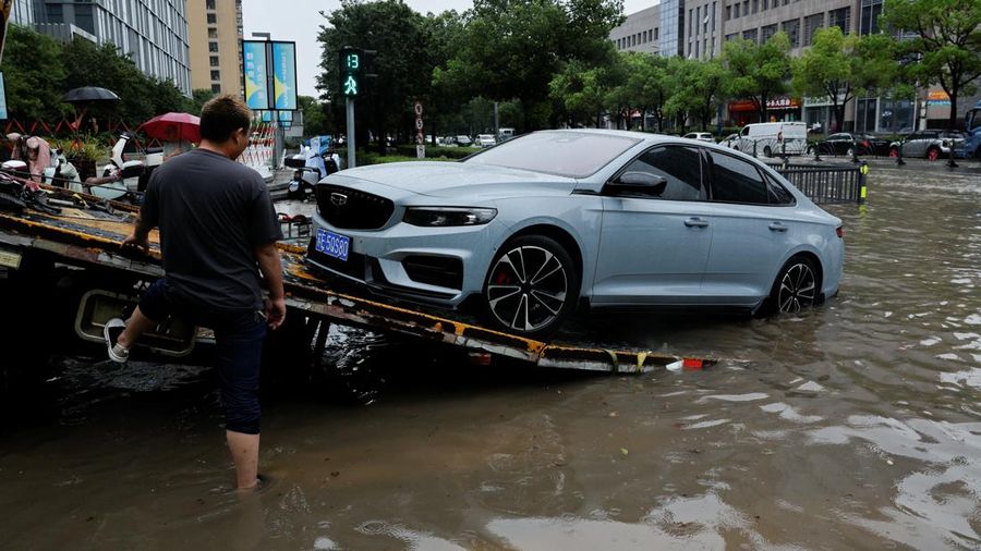 Seorang pekerja menaikkan mobil yang mogok ke atas truk pengangkut mobil di jalan yang tergenang air setelah Topan Dolphin membawa hujan lebat ke Shanghai, Tiongkok, pada 10 Agustus 2026.