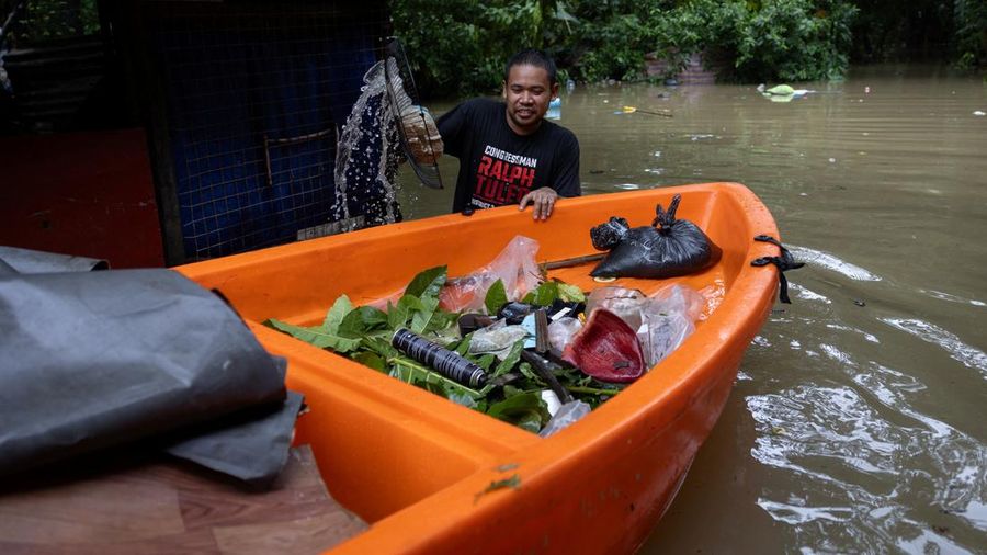 Seorang pria mengumpulkan sampah menggunakan alat penyaring darurat di sebuah desa yang terendam banjir akibat hujan monsun barat daya di Bagong Silangan, Quezon City, Filipina, pada 10 Agustus 2026.