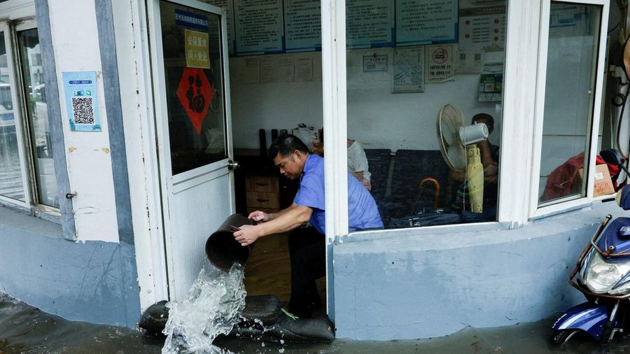 Seseorang menggunakan ember untuk mengeluarkan air dari ruangan yang terendam banjir setelah Topan Dolphin membawa hujan lebat ke Shanghai, Tiongkok, pada 10 Agustus 2026.