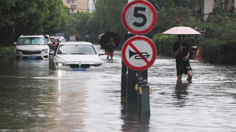 Warga berjalan menerjang jalanan yang tergenang banjir setelah Topan Dolphin membawa hujan lebat ke Shanghai, Tiongkok, pada 10 Agustus 2026.