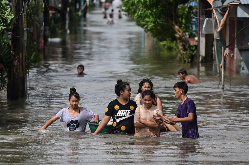 Warga yang membawa barang-barang mereka berjalan menerjang banjir di sebuah desa di tengah hujan monsun barat daya di Bagong Silangan, Quezon City, Filipina, pada 10 Agustus 2026. (REUTERS/Eloisa Lopez)