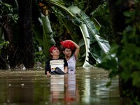 Warga yang membawa barang-barang mereka berjalan menerjang banjir di sebuah desa di tengah hujan monsun barat daya di Bagong Silangan, Quezon City, Filipina, pada 10 Agustus 2026. (REUTERS/Eloisa Lopez)