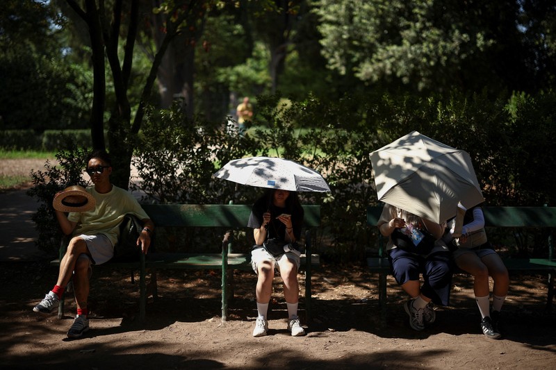 Seorang wanita menggunakan payung untuk berlindung dari terik matahari saat mengunjungi Forum Romawi di tengah suhu yang mendekati 40 derajat Celsius akibat gelombang panas, di Roma, Italia, pada 11 Agustus 2026. (REUTERS/Guglielmo Mangiapane)
