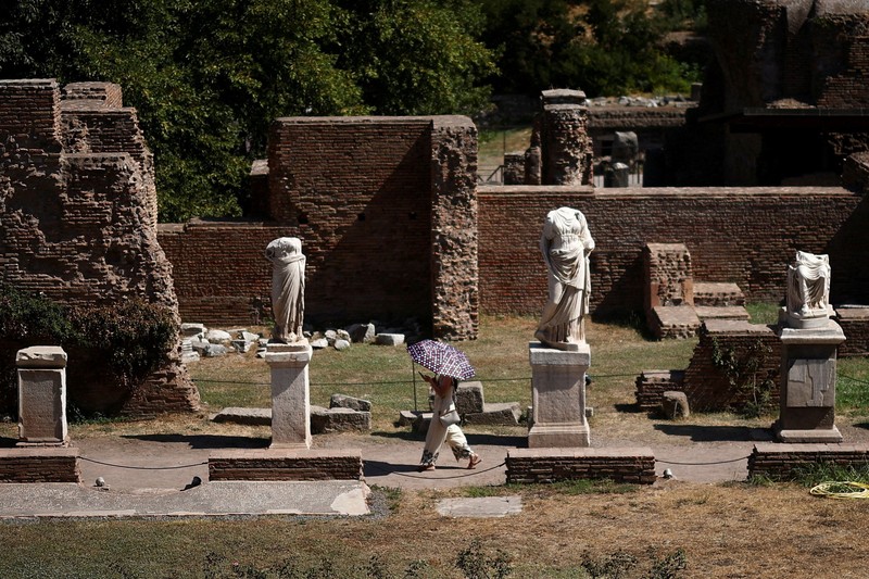 Seorang wanita menggunakan payung untuk berlindung dari terik matahari saat mengunjungi Forum Romawi di tengah suhu yang mendekati 40 derajat Celsius akibat gelombang panas, di Roma, Italia, pada 11 Agustus 2026. (REUTERS/Guglielmo Mangiapane)